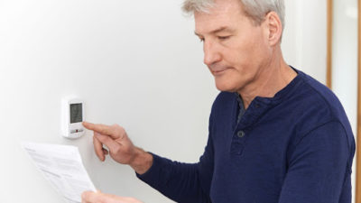 man operating thermostat and looking at manual