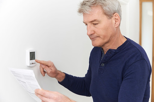man operating thermostat and looking at manual